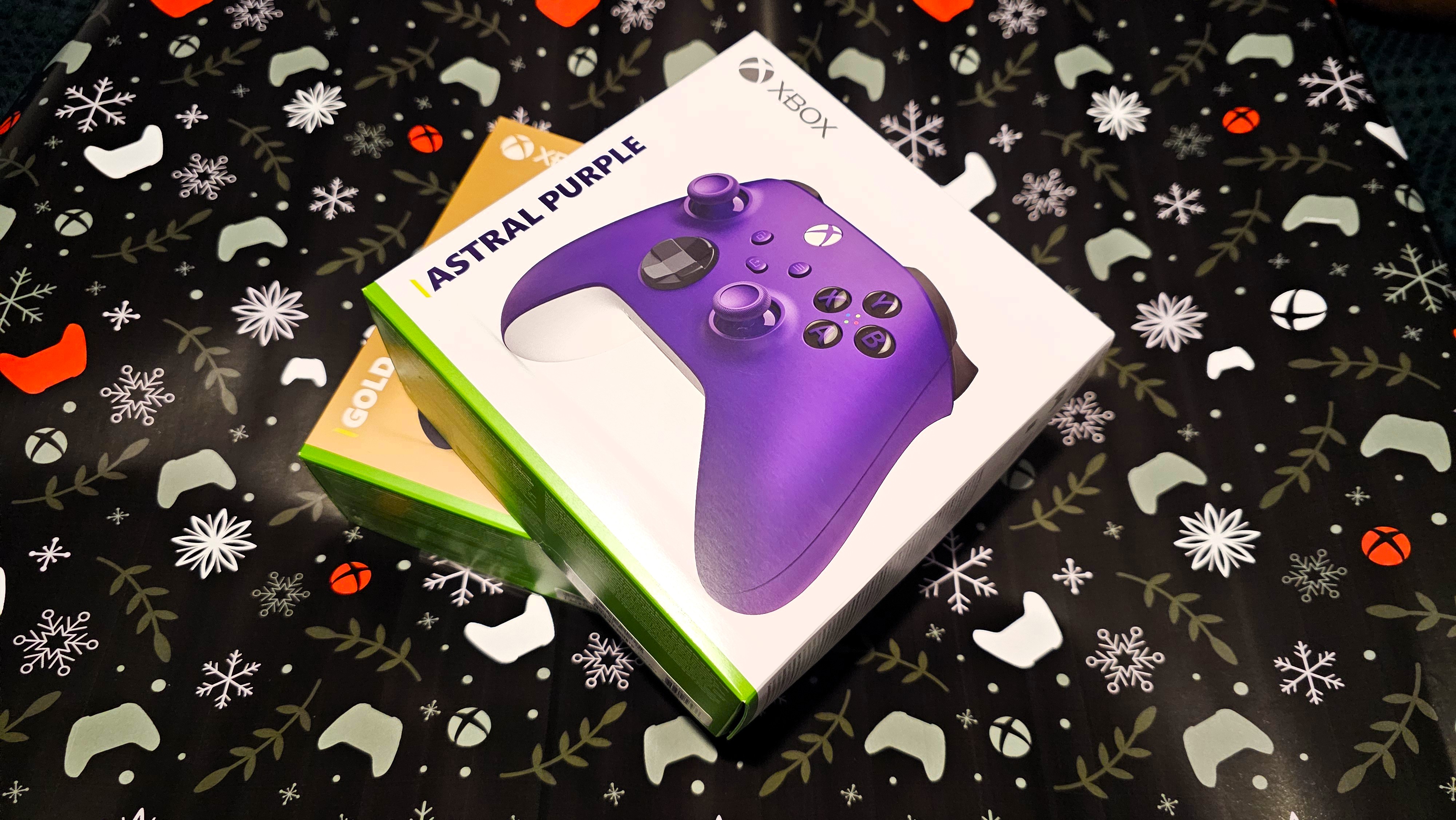 A purple Xbox controller and a gold xbox controller being wrapped in gift paper